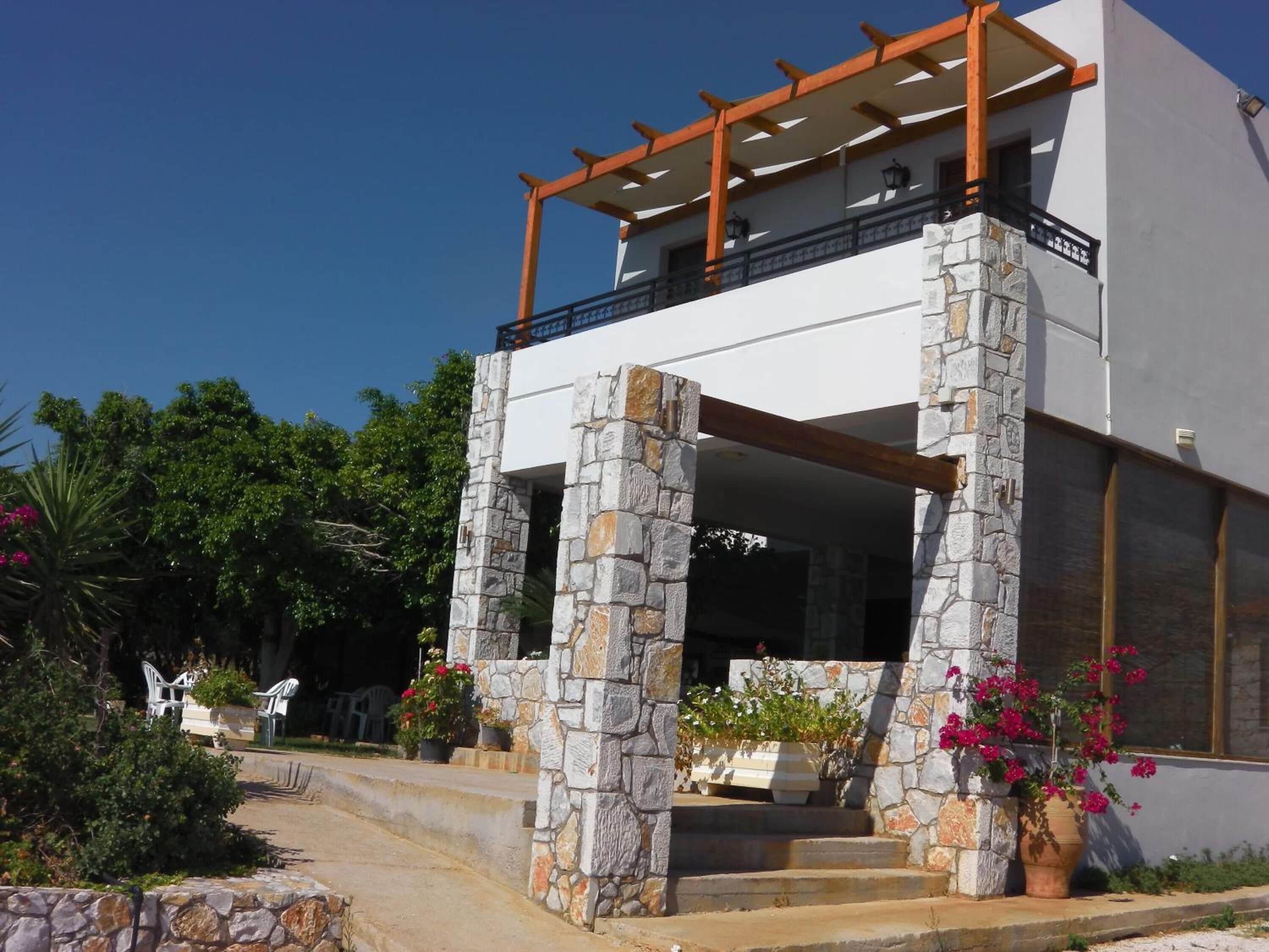 A modern two-story building with stone pillars, a balcony, and a staircase leading to the entrance.