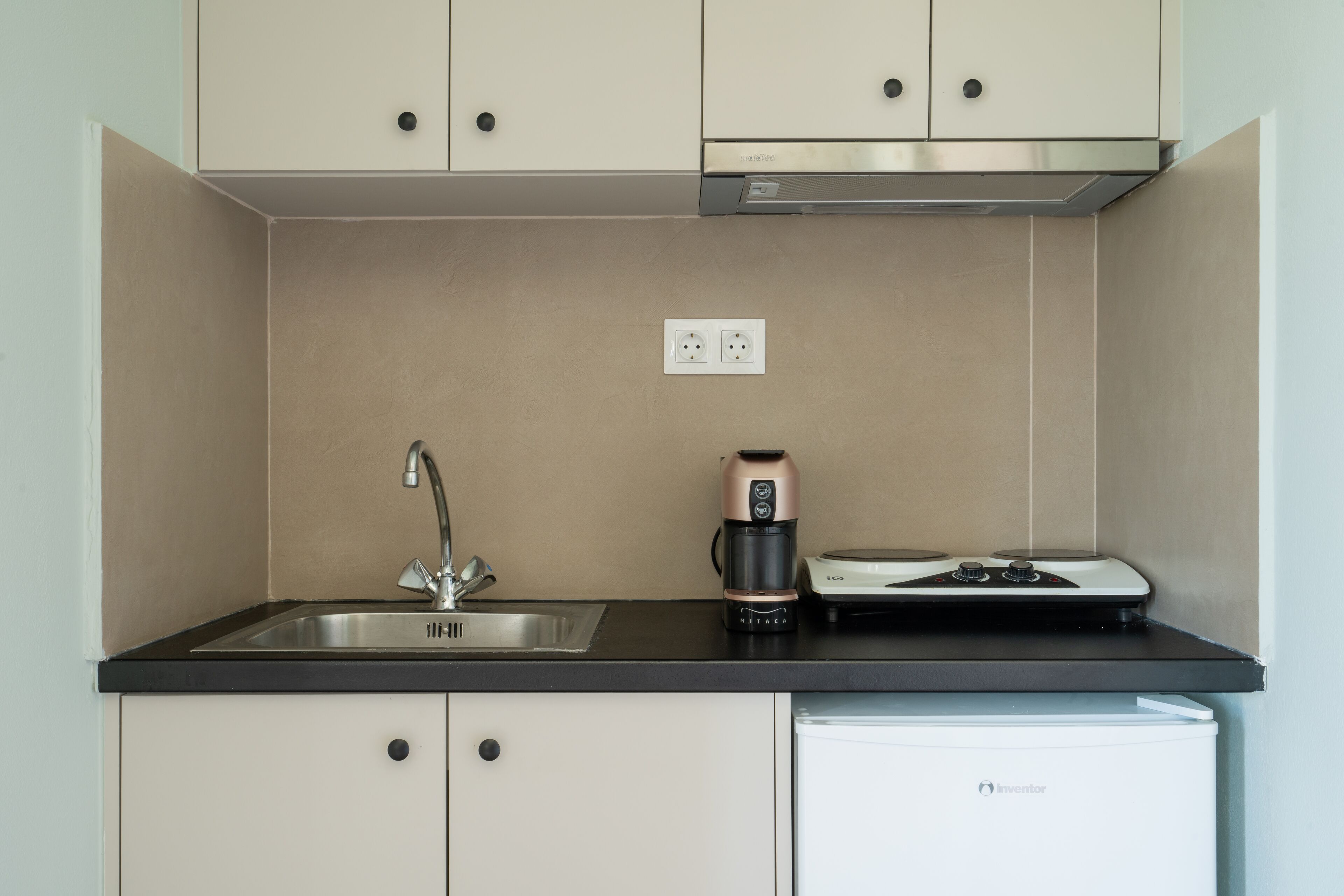 Una kitchenette compacta con un lavamanos, una cafetera y un refrigerador pequeño.