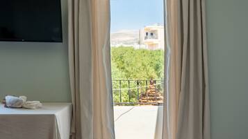 A room with a flat-screen TV, a table with a white tablecloth, and a view of greenery and buildings outside.