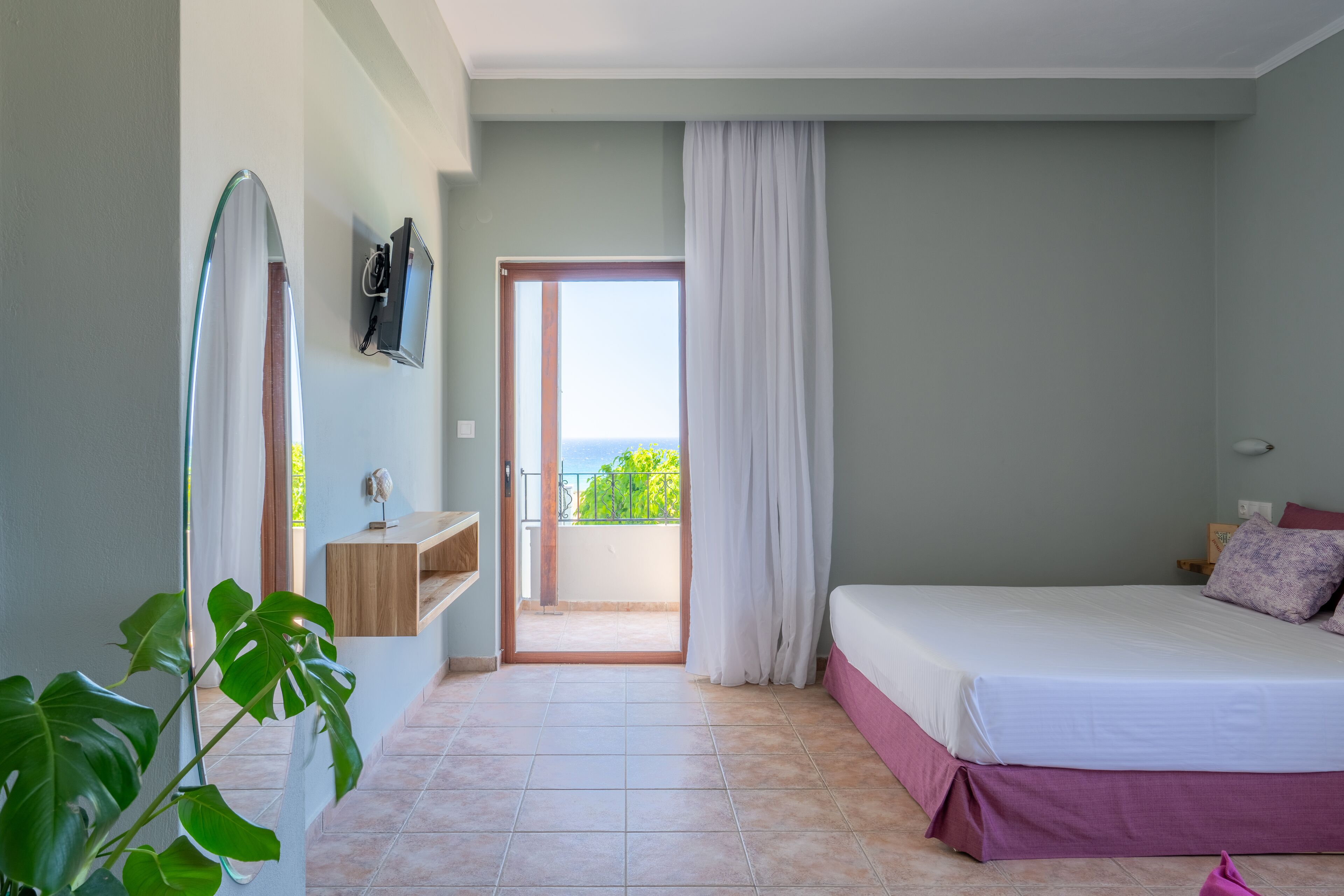 Une chambre avec un lit, une télévision, une plante et un balcon offrant une vue agréable.