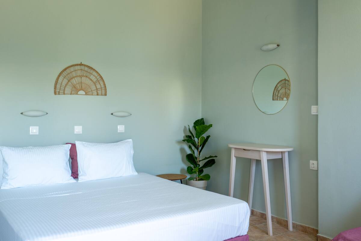 Un dormitorio con cama, un espejo redondo, una mesita pequeña y una planta en maceta.