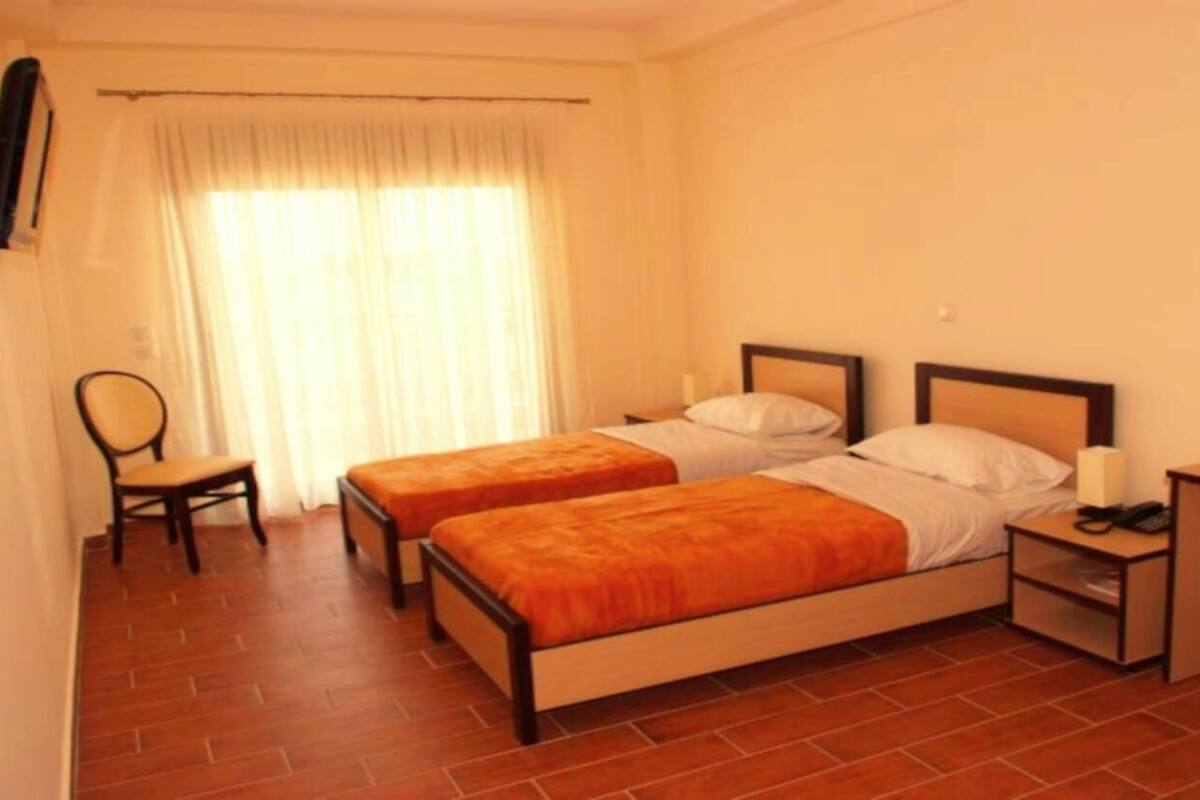 Ein Hotelzimmer mit zwei Einzelbetten, einem Schreibtisch, einem Stuhl und einem kleinen Tisch.