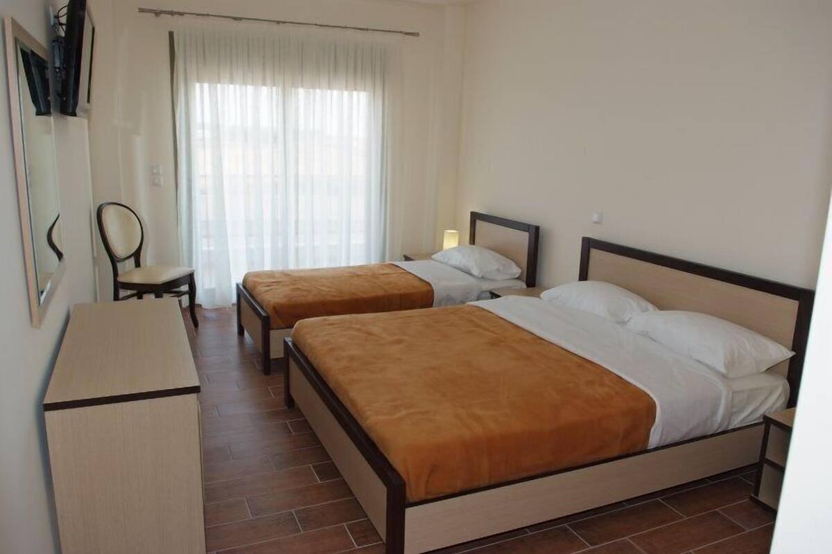 Ein Hotelzimmer mit zwei Einzelbetten, einem Schreibtisch, einem Stuhl und einem Fenster mit Vorhängen.