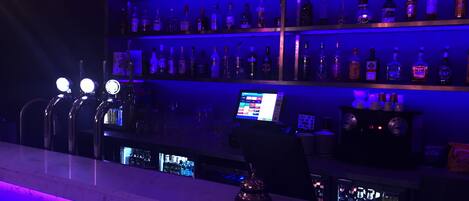 A bar area with multiple shelves of liquor bottles, a digital menu display, and a bar counter.