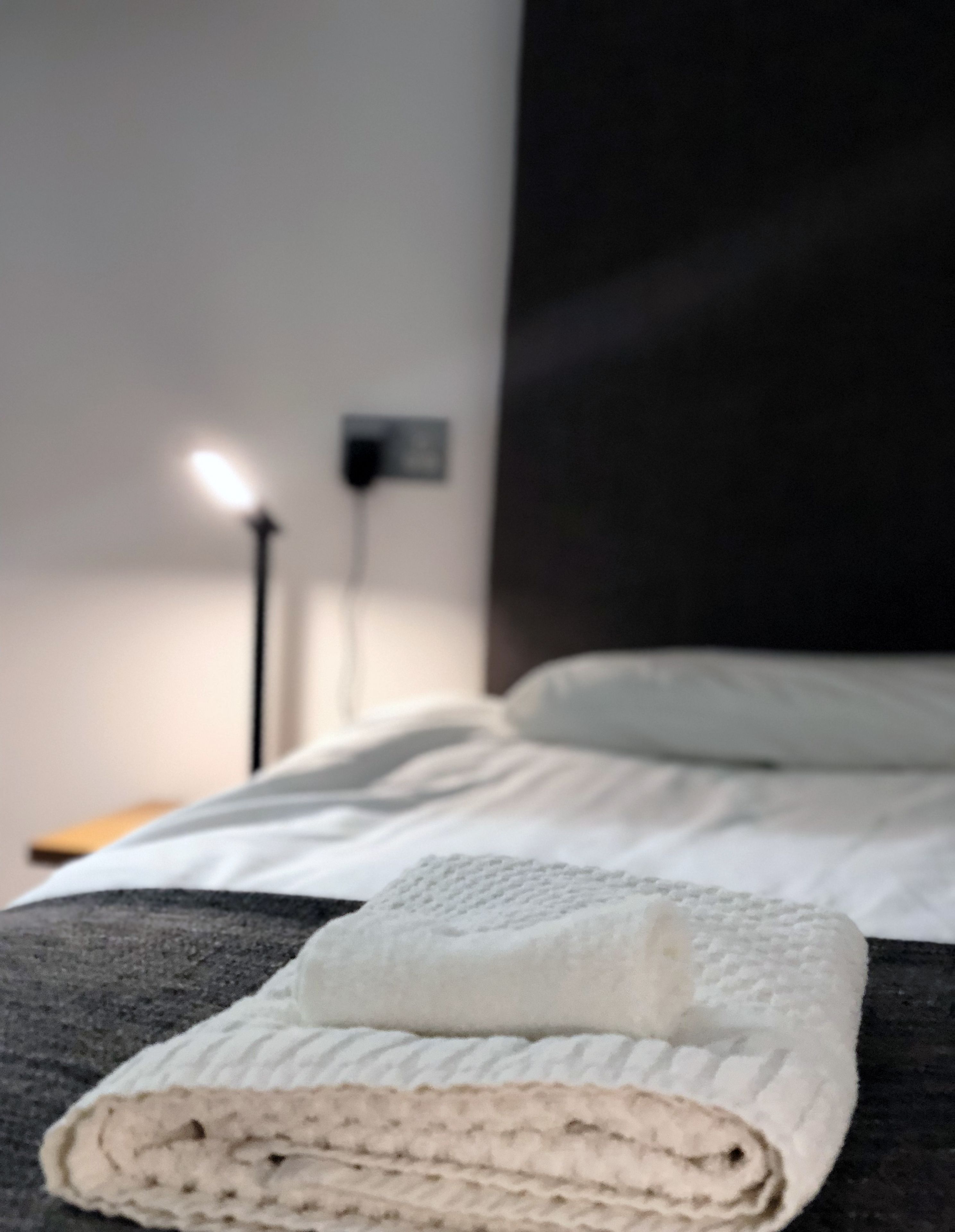 A neatly made bed with white bedding and a rolled towel.