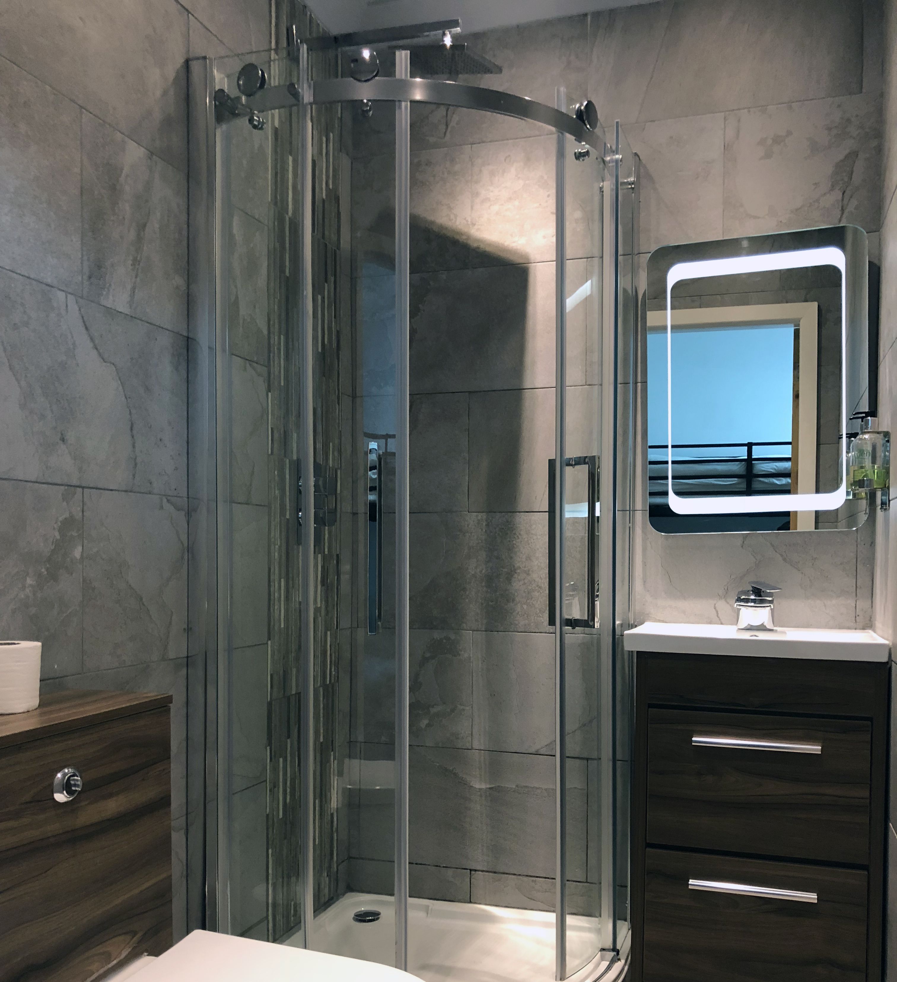 A modern bathroom with a glass-enclosed shower, a vanity with a mirror, and a marble-tiled wall.