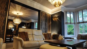 A well-lit living room with a large sofa, a coffee table, and a chandelier. - Tir-y-Coed Country House (Conwy)