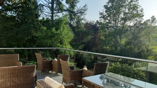 A deck with wicker furniture and a glass-top table, surrounded by lush greenery. - Tir-y-Coed Country House (Conwy)