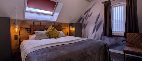 A bedroom with a large bed, a skylight, a window with curtains, and a wooden headboard.