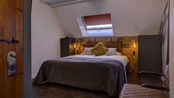 A bedroom with a sloped ceiling, a skylight, a bed with a headboard, a chair, and a wooden floor.