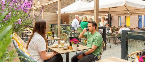An outdoor café with wooden tables and chairs, surrounded by greenery and flowers.