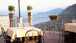A terrace with tables set for dining, chairs, potted plants, and a view of the sea. - Agostiniana Hotel (Forza d'Agro)