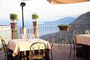 A terrace with tables set for dining, chairs, potted plants, and a view of the sea. - Agostiniana Hotel (Forza d'Agro)