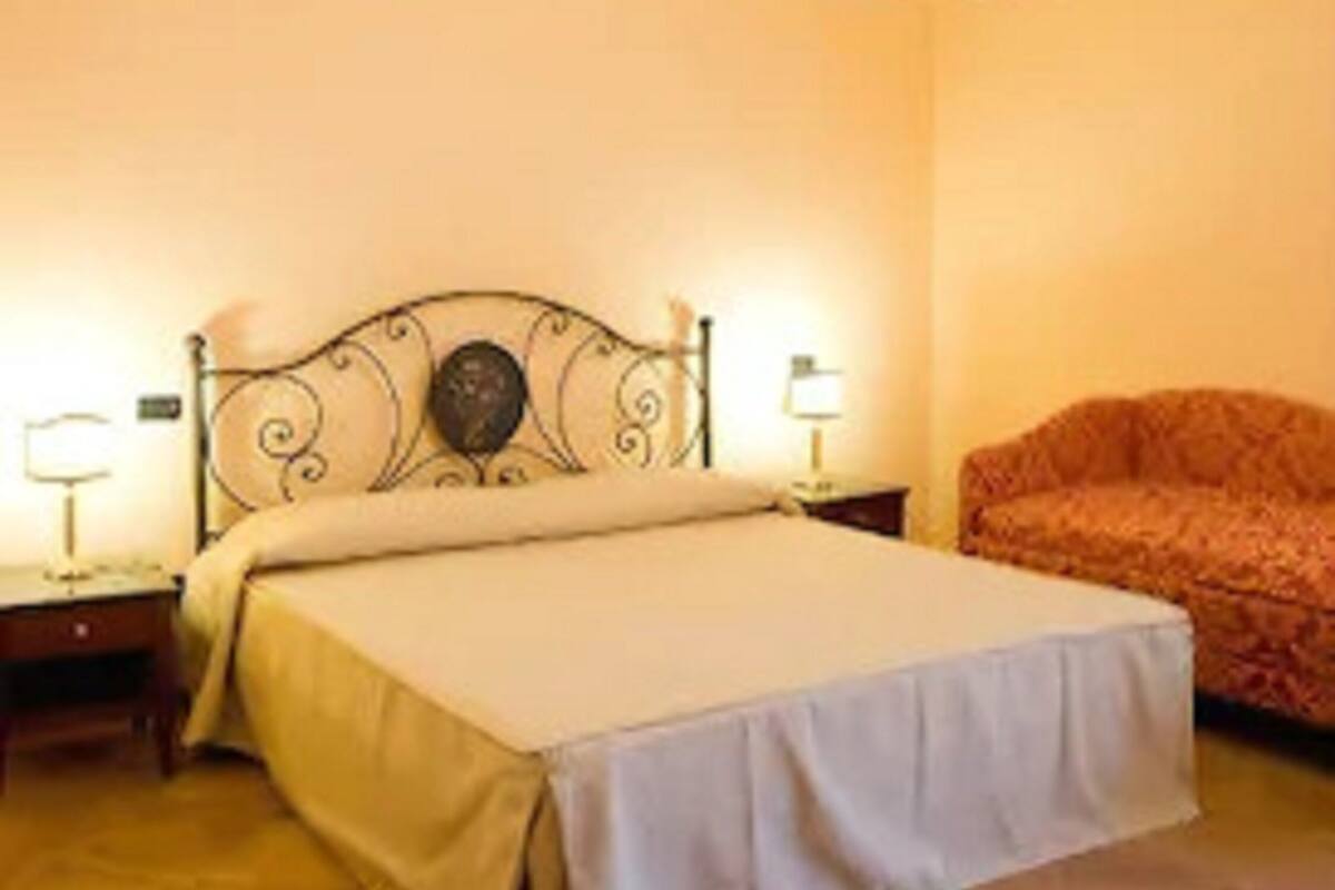 A bedroom with a bed, a nightstand, a lamp, a sofa, and a chandelier.