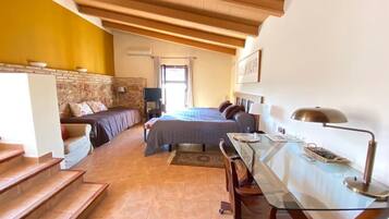 A spacious room with a bed, a desk with a lamp, and a sofa.