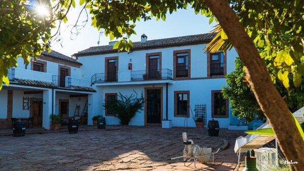 A courtyard with a building featuring a tiled roof, multiple windows, and balconies. - Molino la Nava (Montoro)