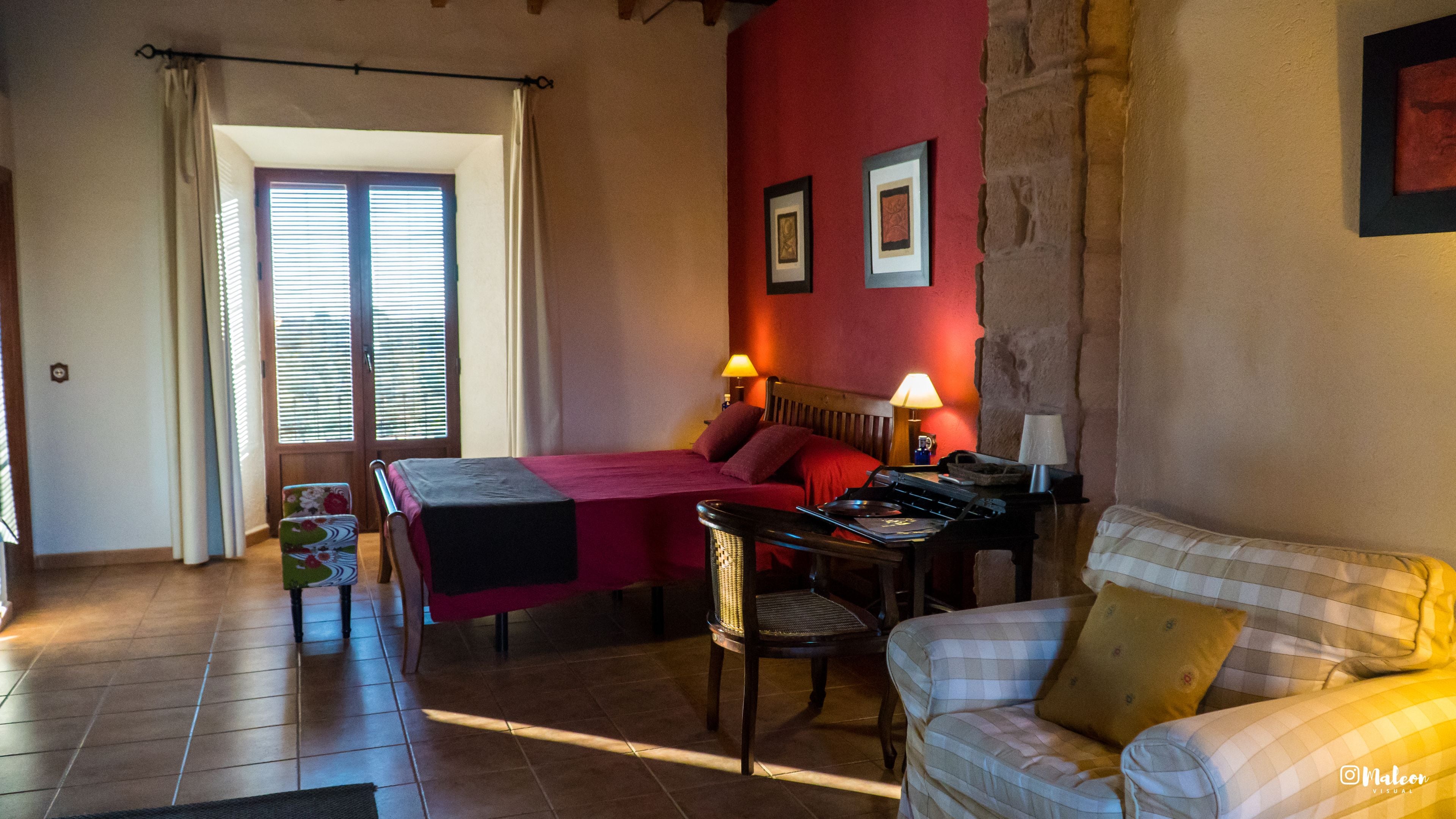 A hotel room with a bed, a desk, a chair, a sofa, and a window with curtains.