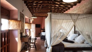 Un dormitorio con cama de dosel, vigas de madera en el techo, un escritorio con silla y un televisor en la pared.
