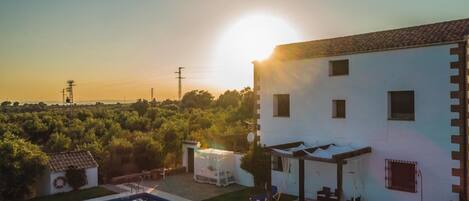 Vista a la piscina d'una vila amb piscina, un porxo cobert i una vista del capvespre sobre una zona boscosa.