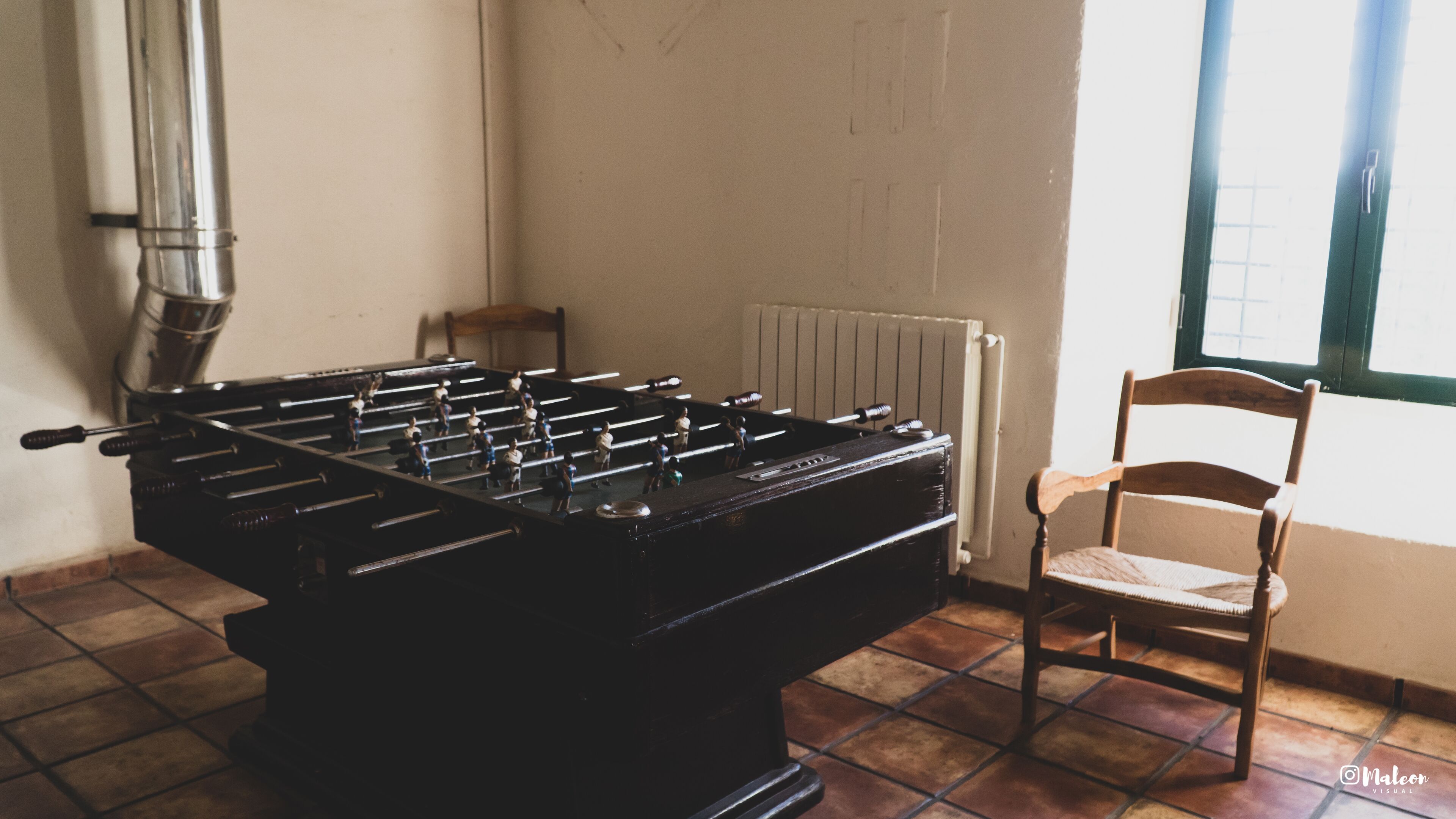 Een tafelvoetbaltafel in een ruimte met betegelde vloer, een radiator en een raam.