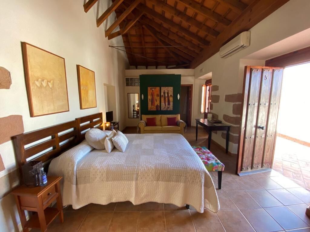 Une chambre à coucher avec un lit en bois, une table de chevet, un banc et des œuvres d’art accrochées aux murs.