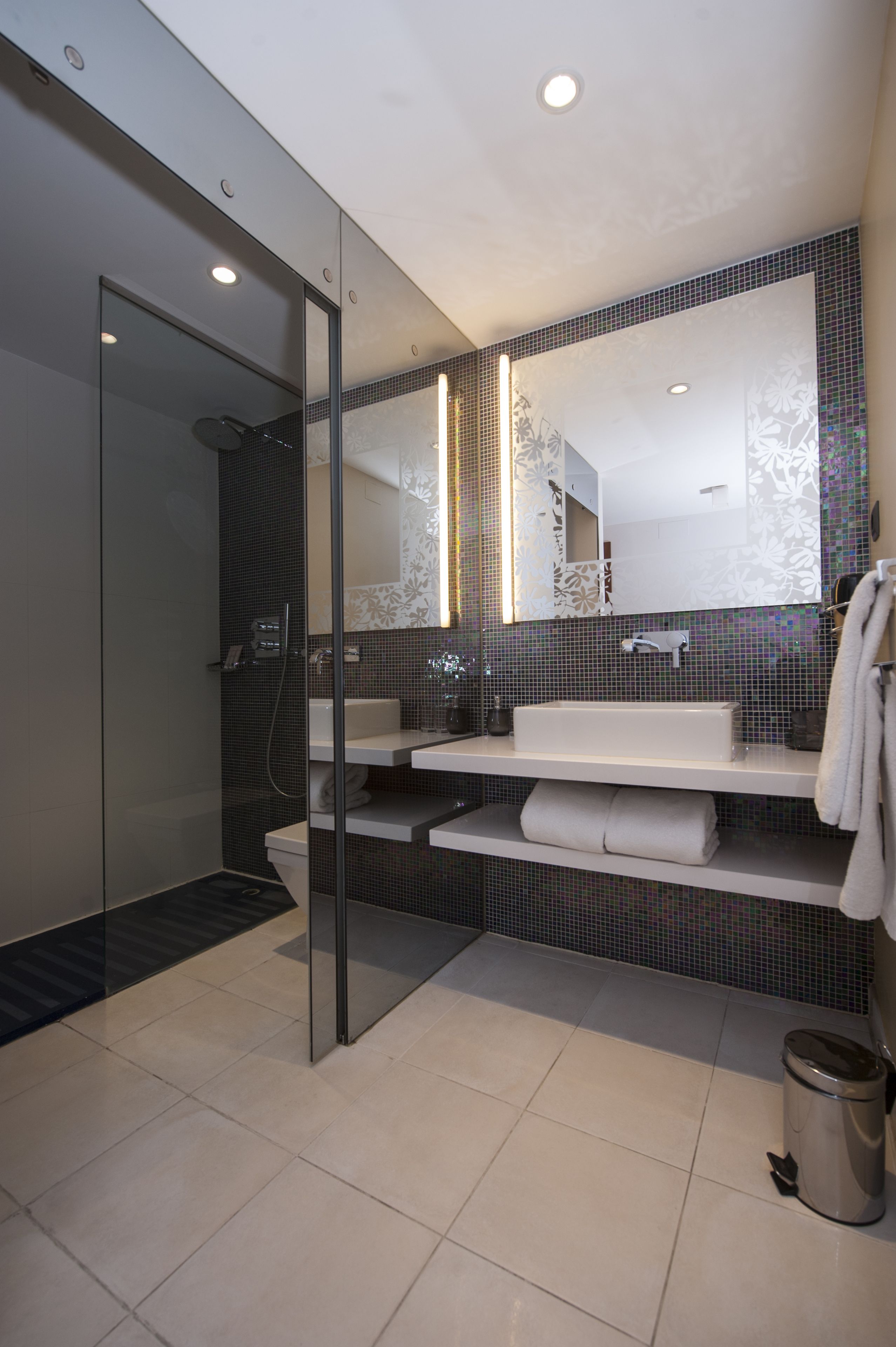 Un baño moderno con cabina de ducha de vidrio, un lavabo blanco y un espejo grande.