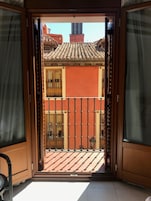 An open door leading to a balcony with a tiled roof and a view of a building with a red facade.
