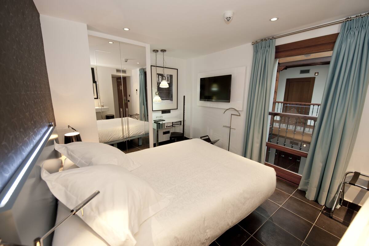 A hotel room with a large bed, a TV mounted on the wall, a balcony with a railing, and a bathroom with a mirror and sink.