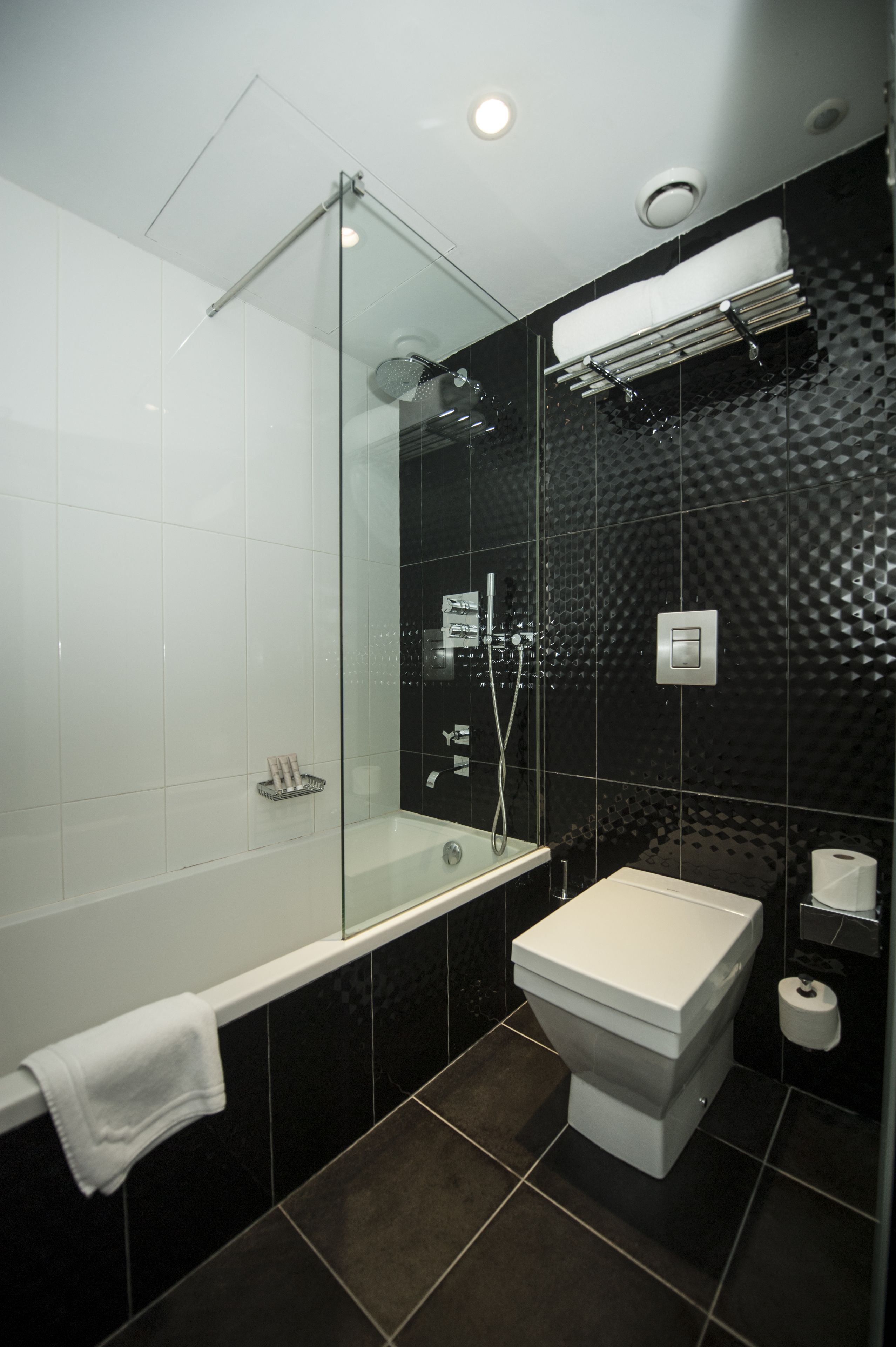 Een moderne badkamer met een glazen douchecabine, een witte badkuip en een toilet.