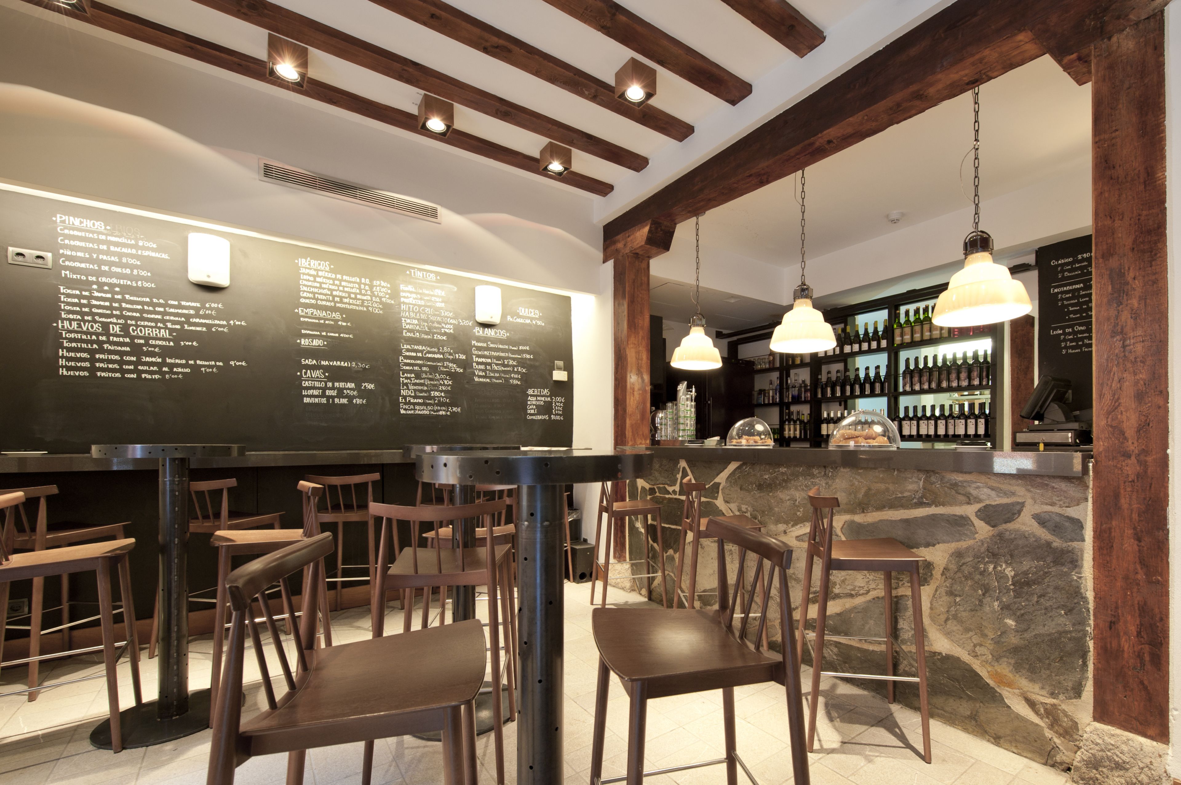 Interior de restaurante com cadeiras de madeira, balcão de pedra e luminárias pendentes.