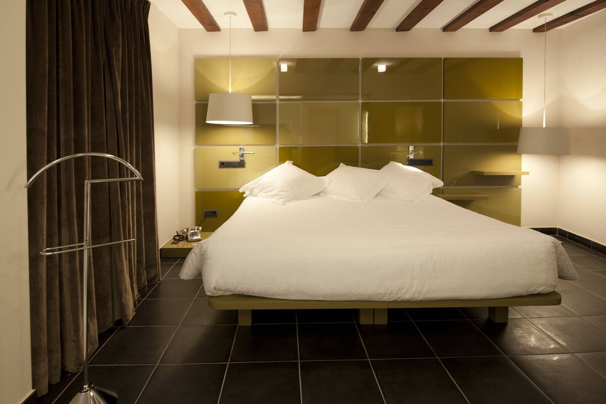 A modern hotel room with a large bed, a mirror wall, and a floor lamp.