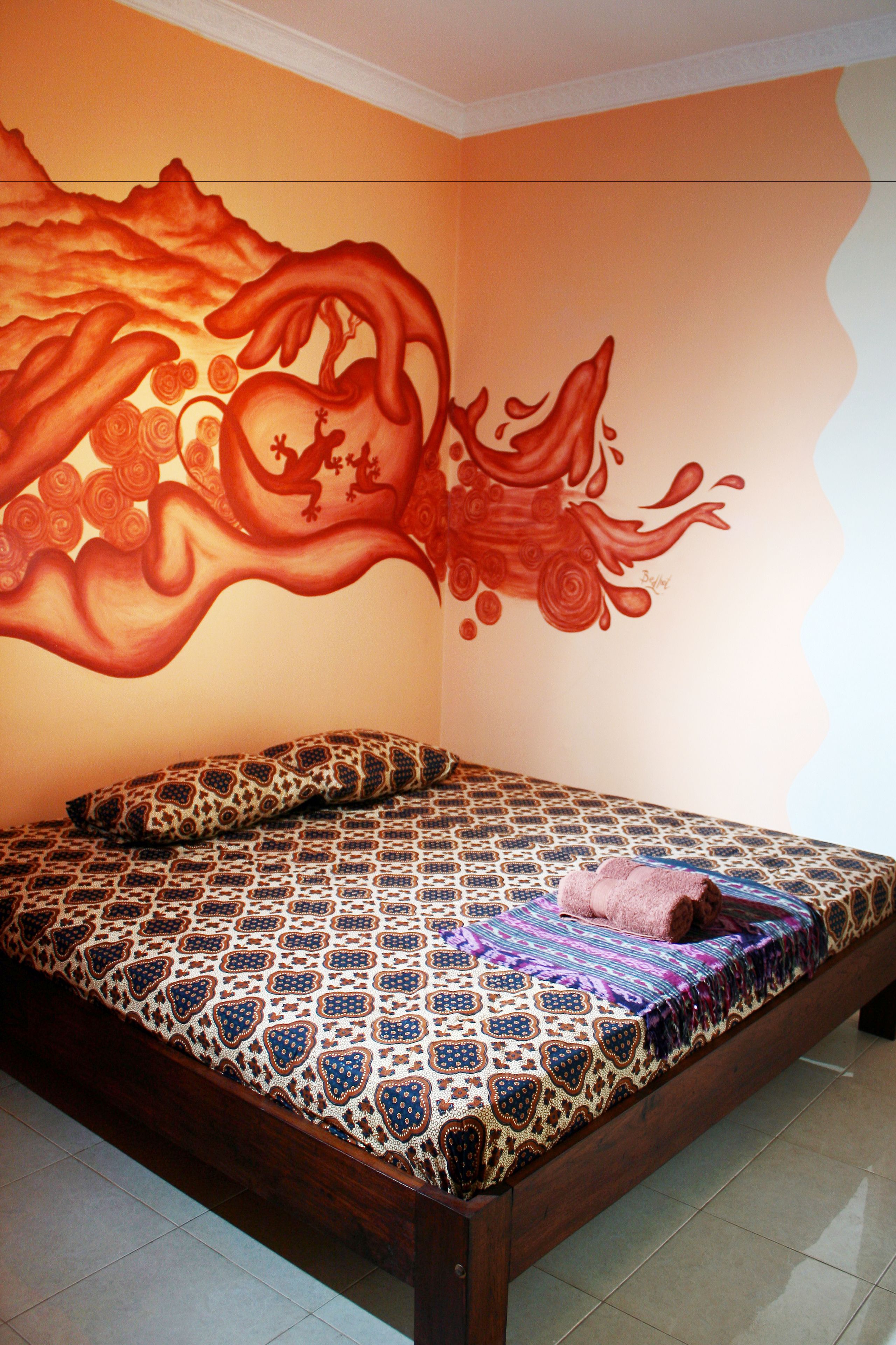 A bedroom with a patterned bedspread, a pillow, and a wall mural.