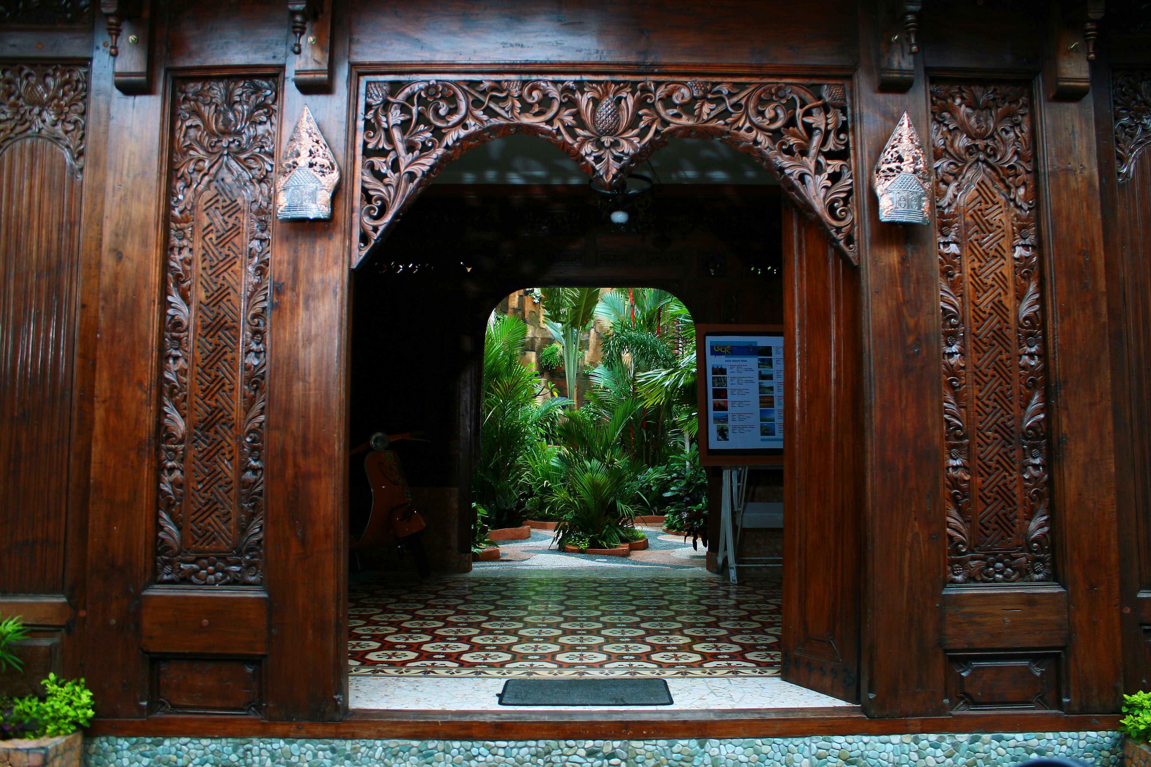 An ornate wooden entrance with intricate carvings and a tiled floor leading to a lush garden area.