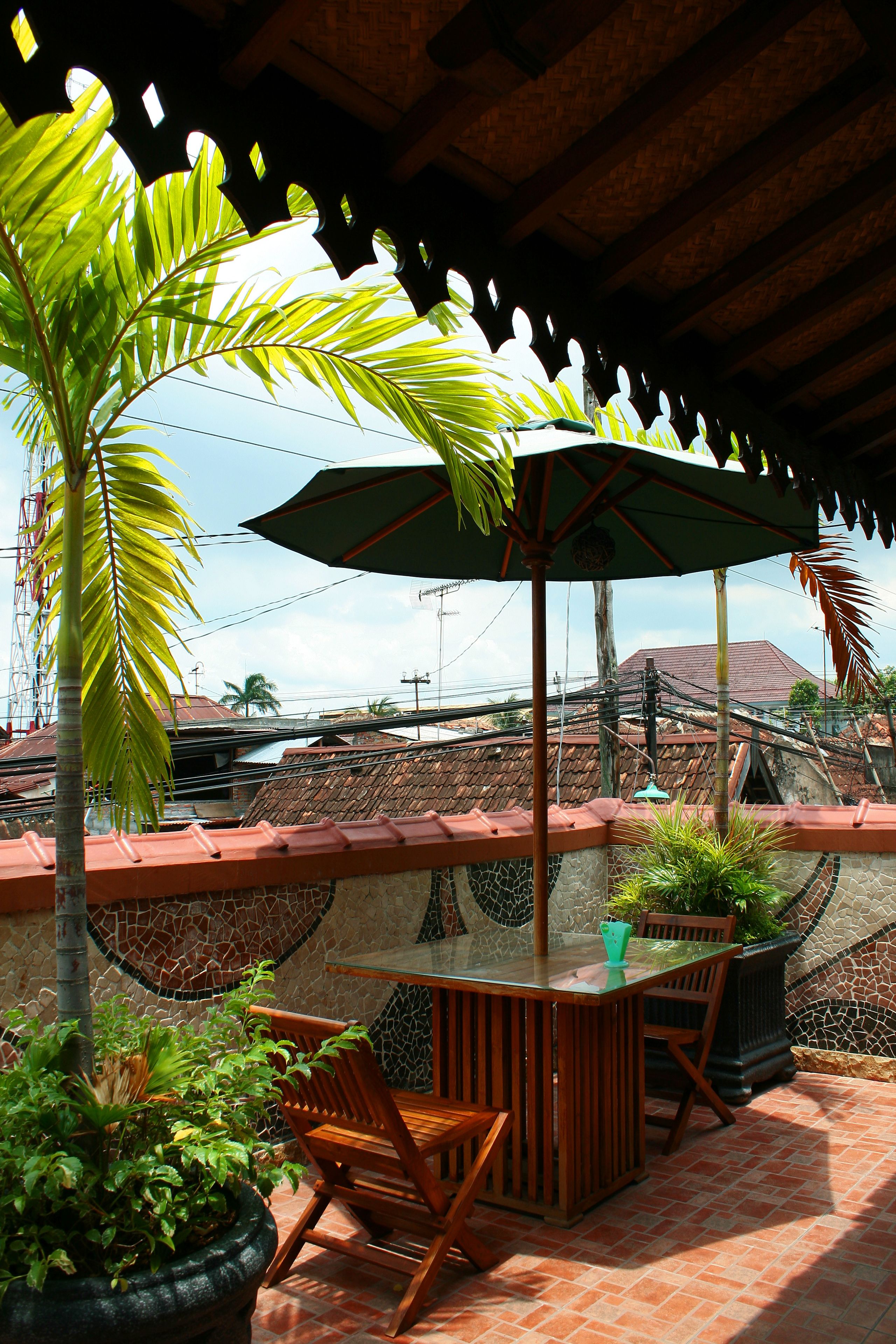 An outdoor patio with a table and chairs, surrounded by potted plants and a decorative umbrella.