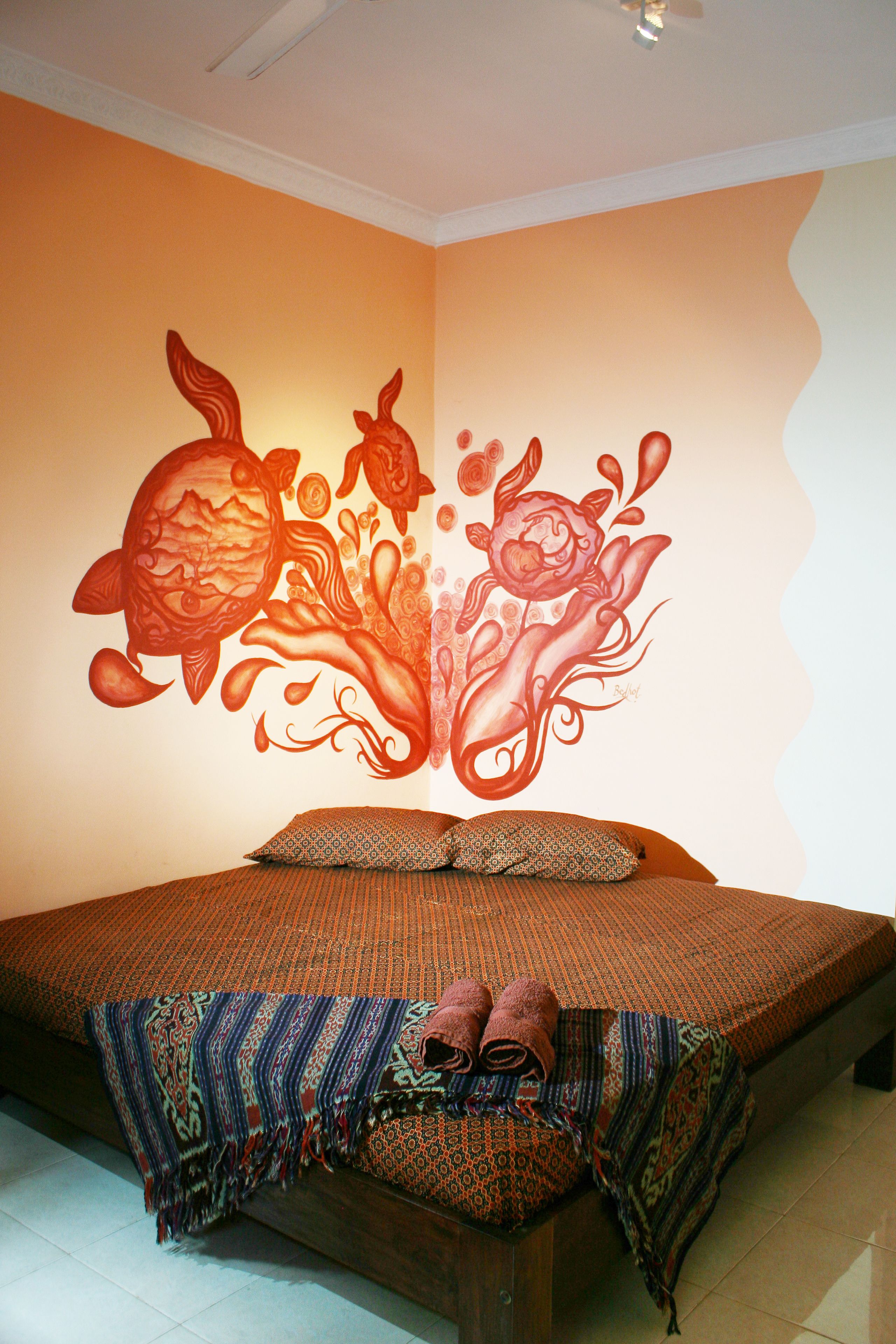 A bedroom with a bed, patterned bedding, and a wall mural.