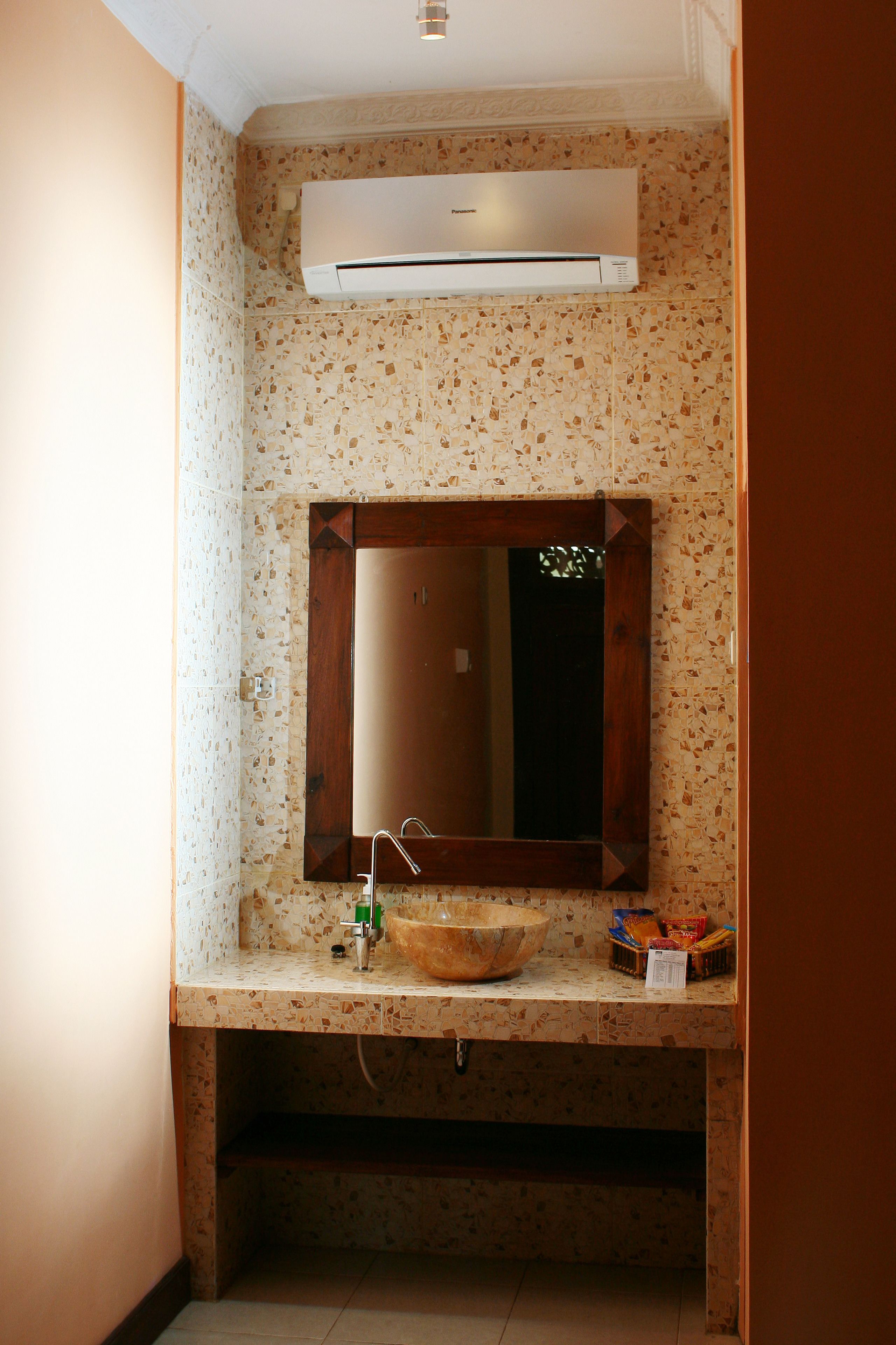 A bathroom with a freestanding sink, a mirror, and an air conditioning unit above.
