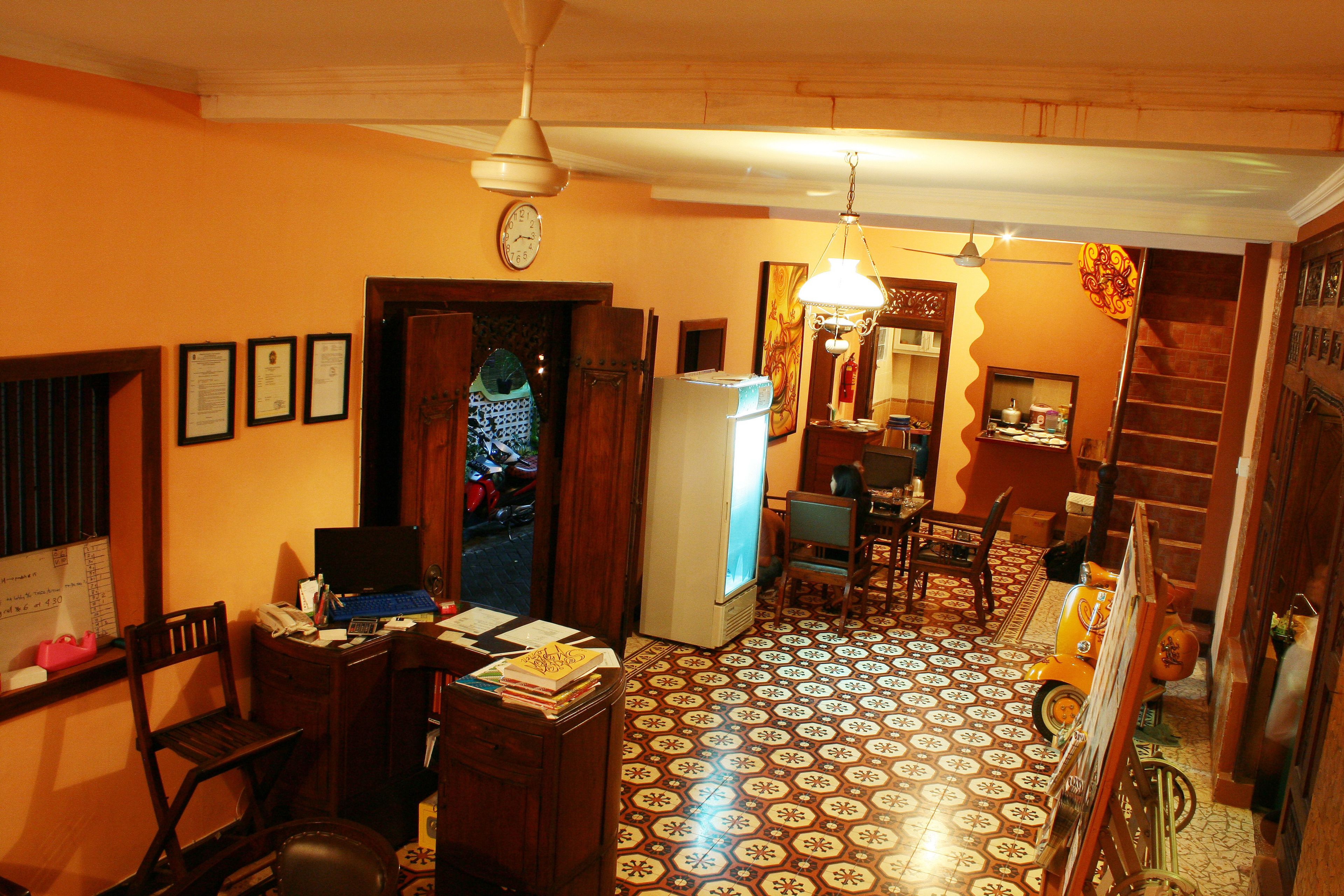 A room with a desk, chair, and a computer. There is a refrigerator, a clock on the wall, and a patterned floor.