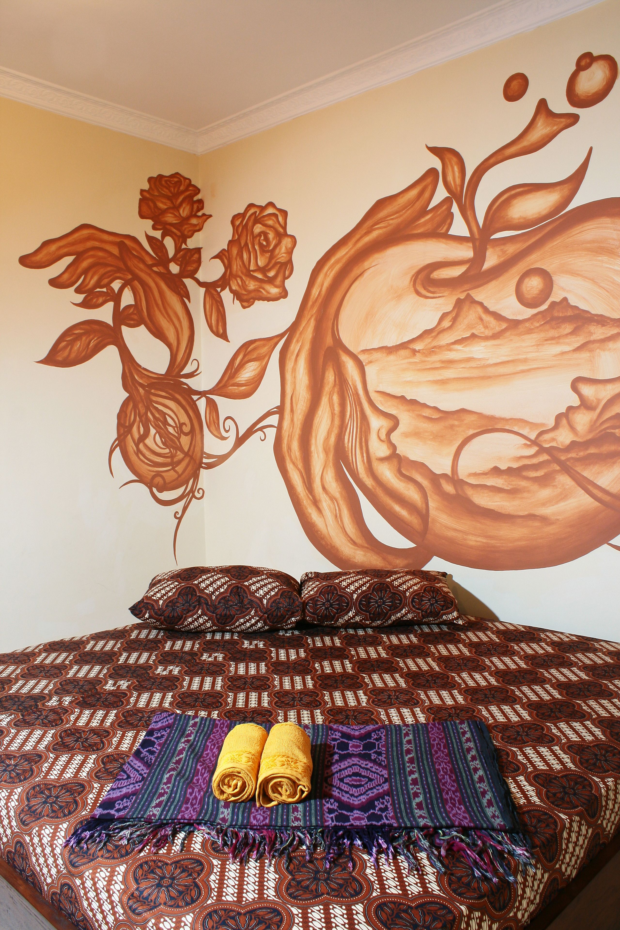 A bed with patterned bedding, a wall mural, and two rolled towels.