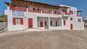 A two-story white building with red accents, a sign for Hotel Smaragdi, and a covered outdoor area.