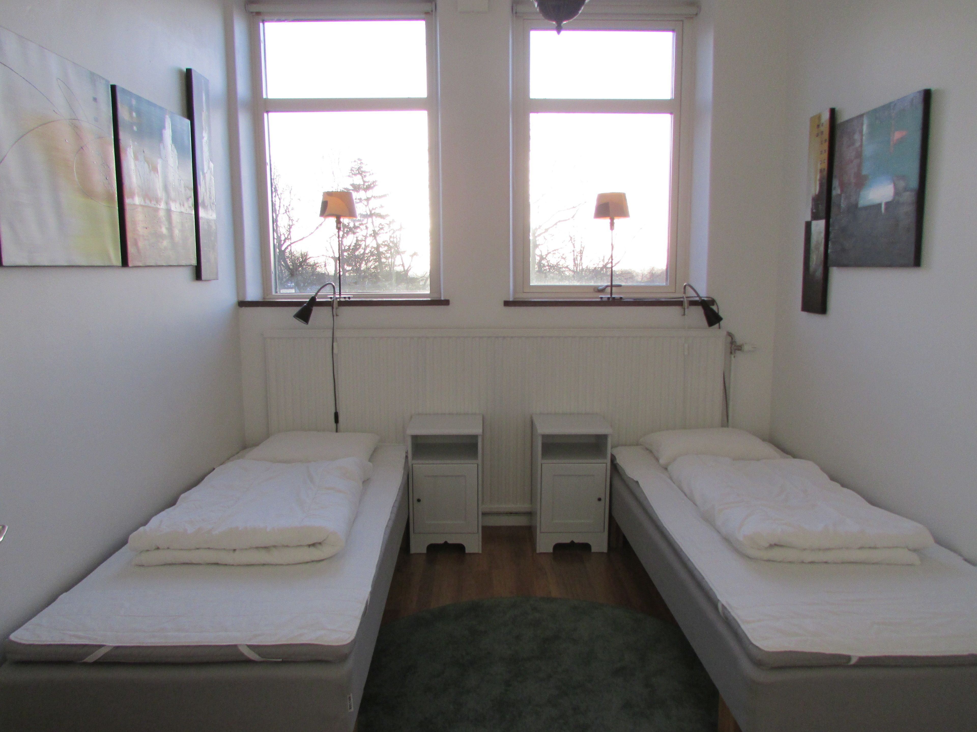 A twin room with two single beds, a window, a radiator, and a small bedside table with a lamp.