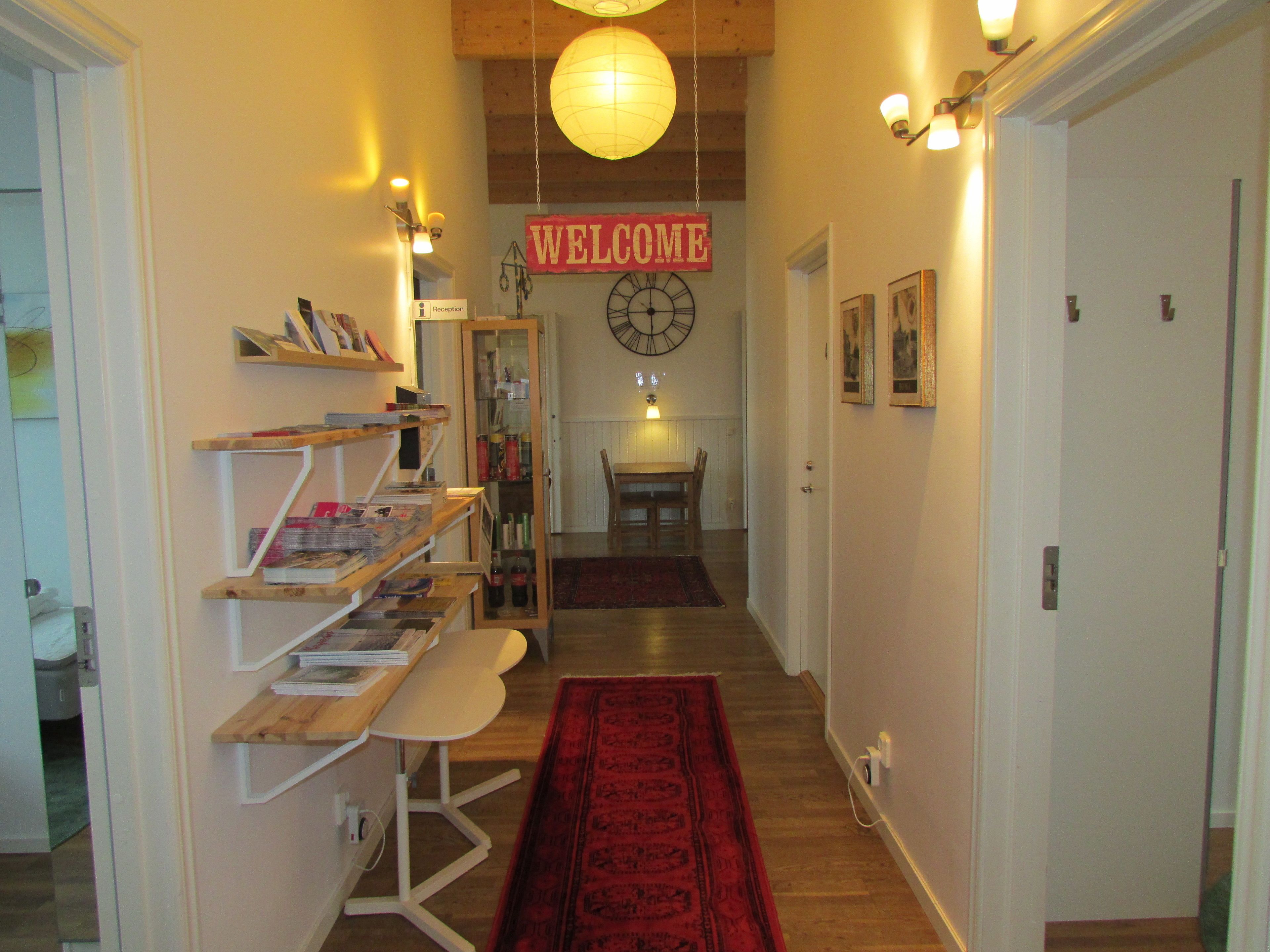 A hallway with a red carpet, a reception desk, a 'Welcome' sign, and a clock on the wall.