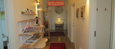 Un pasillo con alfombra roja, un mostrador de recepción, un letrero que dice 'Welcome' y un reloj en la pared.