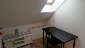 Een kleine kamer met schuine wanden, een dakraam, een bureau met stoel, een klein plankje en een opbergunit.