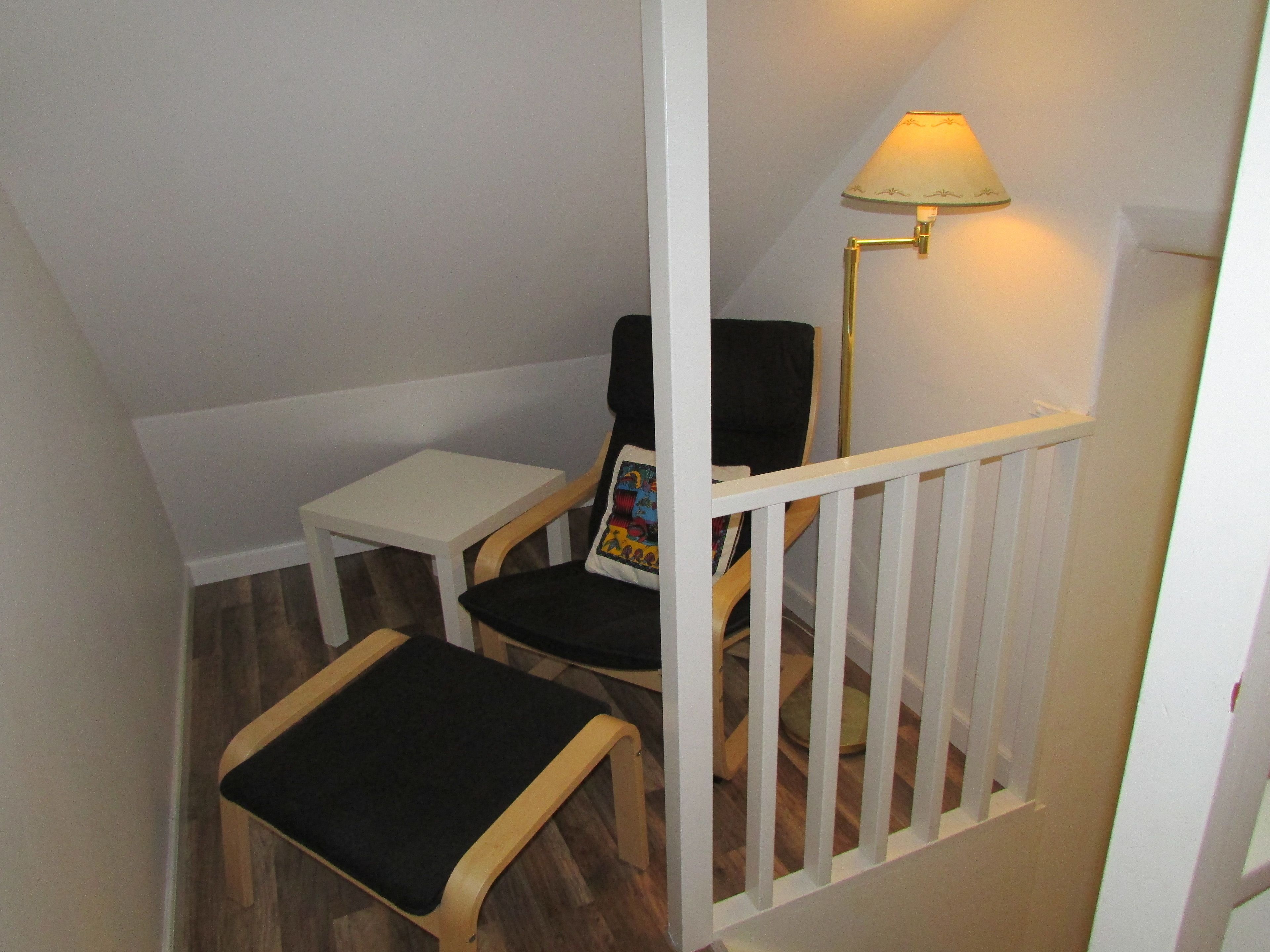 Een kleine kamer met een witte tafel, twee stoelen, een lamp en een witte leuning.