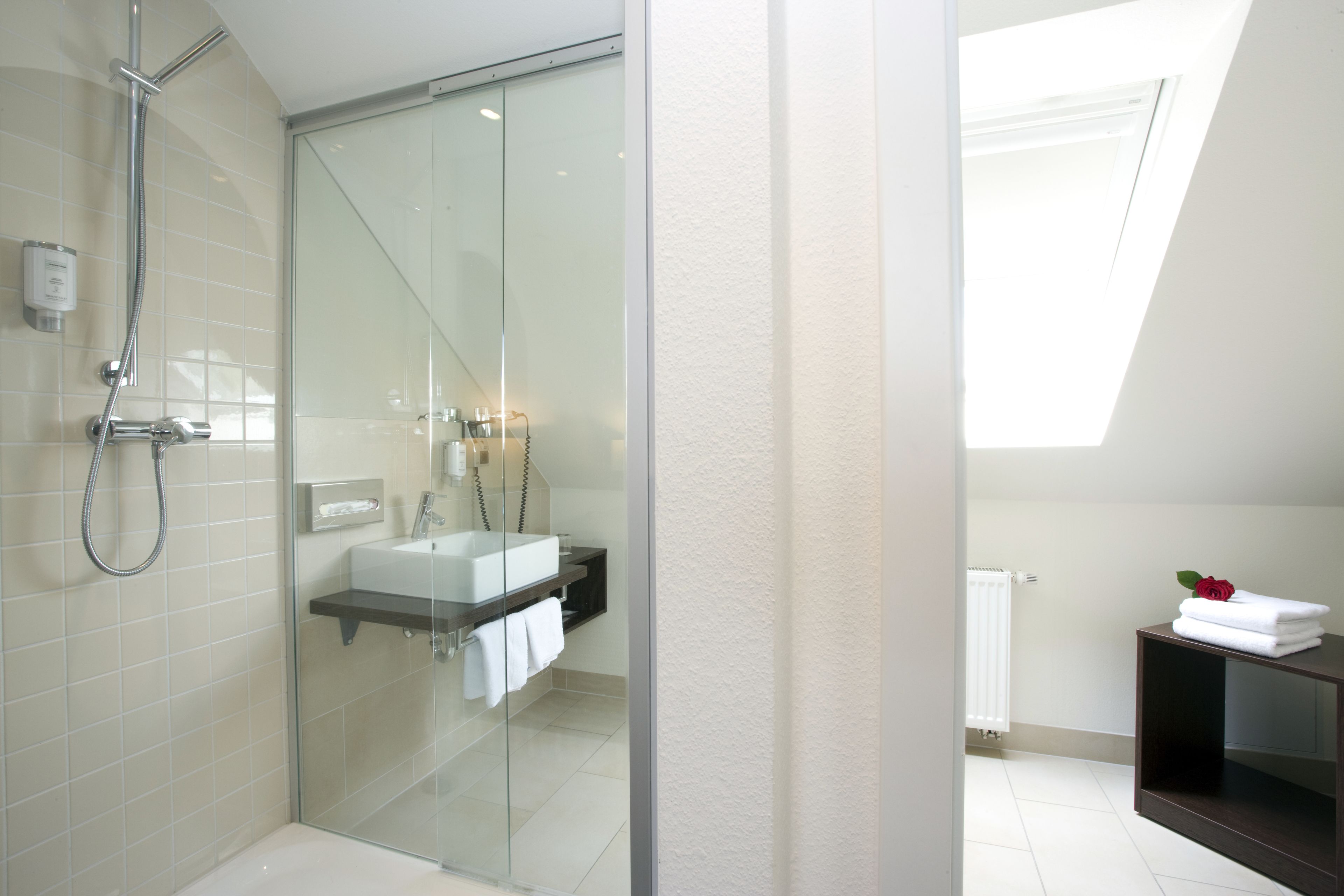 Une salle de bain moderne avec une douche à l’italienne en verre, un lavabo blanc et un meuble-lavabo en bois foncé.