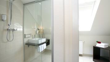 Une salle de bain moderne avec une douche à l’italienne en verre, un lavabo blanc et un meuble-lavabo en bois foncé.