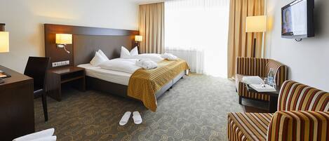 A hotel room with a bed, a desk, a chair, a TV, and a window with curtains.
