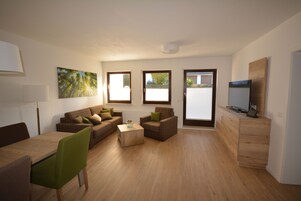 A modern living room with a wooden floor, a green chair, a brown sofa, a wooden coffee table, and a TV on a wooden cabinet.