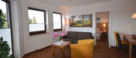 A living room with a sofa, yellow armchair, and a painting on the wall.
