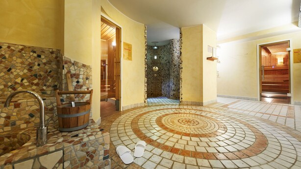 Un baño con piso de mosaicos, un balde de madera y un lavamanos.